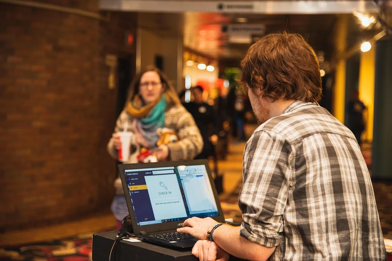 indoors, movie theatre, ticket, ticket check-in, customer, lobby, theatre, movie, computer, scanner, brown computer, brown laptop, brown movie, brown theater, brown check, ticket, lobby, lobby, scanner, scanner, scanner, scanner, scanner