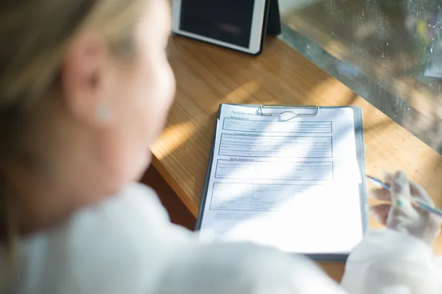 A woman fills out an application form with a pen at a sunlit wooden desk. Kundeoplevelse i Danmark: Sådan måler og styrer du kunderejsen